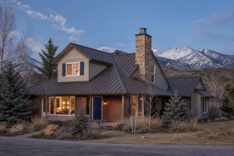 A 1990s mountain modern house with a metal roof with a stone-veneer chimney with a steel cap on an asphalt shingle roof rising above the roof; illustrative image