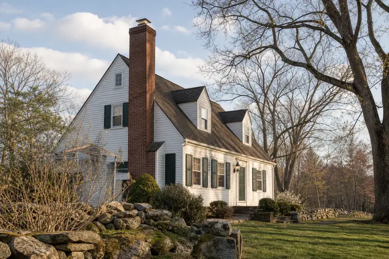 A 1950s Cape-style cottage with a tall brick chimney on a steep gable roof and a stainless steel cap; illustrative image
