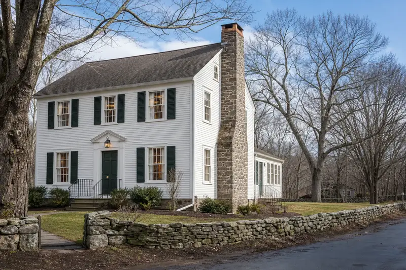 A 1950s white clapboard colonial with a stone masonry chimney and neat, even mortar joints; illustrative image