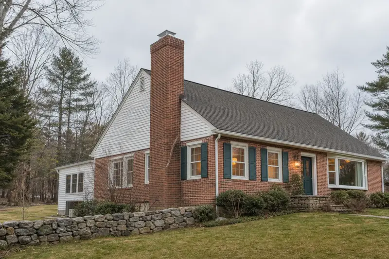 A 1970s brick-front ranch house with a tall brick chimney on a steep gable roof and a stainless steel cap; illustrative image