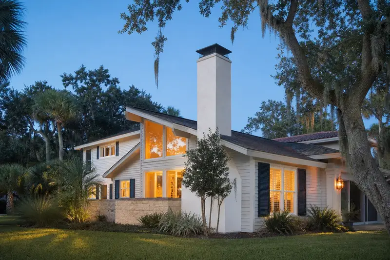 A 1970s coastal contemporary house with lap siding in soft daylight with a stucco-clad masonry chimney with a metal cap standing clear above the roofline; illustrative image