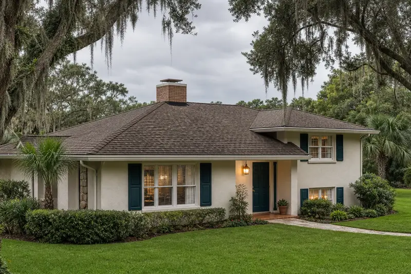 A 1980s split-plan stucco house with a shingle hip roof with a short brick chimney with a concrete crown above a hip roof rising above the roof; illustrative image