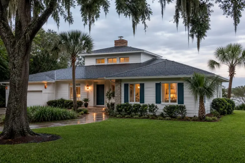 A 1980s coastal contemporary house with lap siding after steady rain with a short brick chimney with a concrete crown above a hip roof and a stainless steel cap; illustrative image