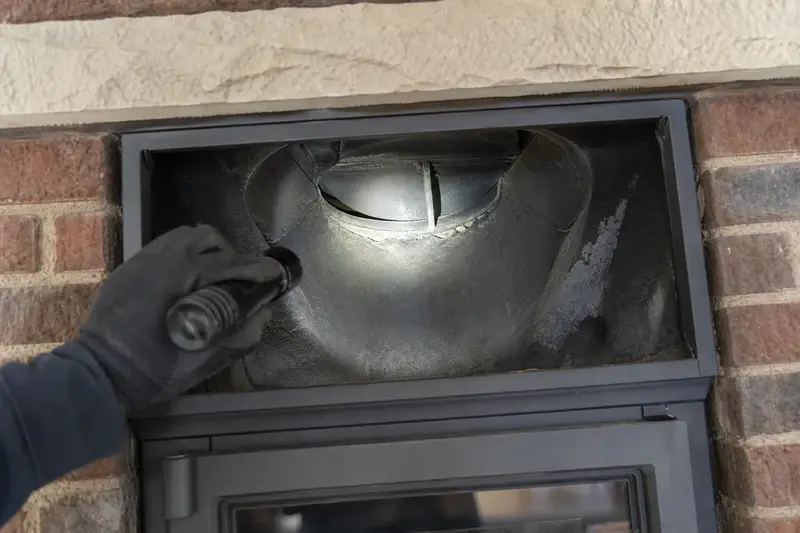 A flashlight beam across the smoke chamber and damper of a wood-burning insert in a brick opening, a gloved hand holding the light; illustrative image