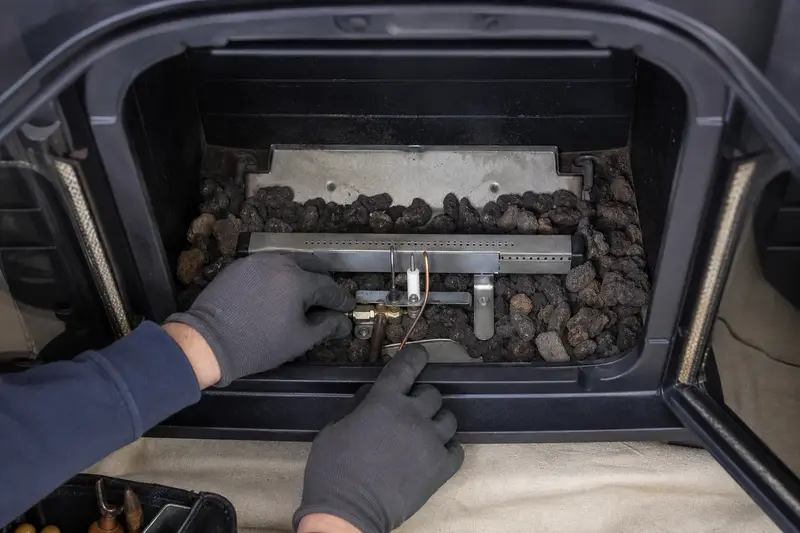 The burner, pilot assembly and ember bed inside a freestanding gas stove, unlit, seen up close; illustrative image