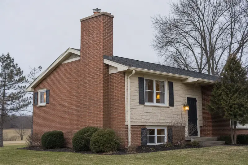 A 1980s split-level house in soft daylight with a red brick chimney with a concrete crown and even brickwork; illustrative image