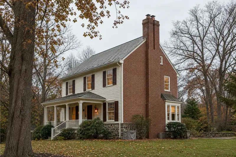 A 1980s two-story suburban house with a front porch with a two-flue brick chimney on a steep gable roof and neat mortar joints; illustrative image