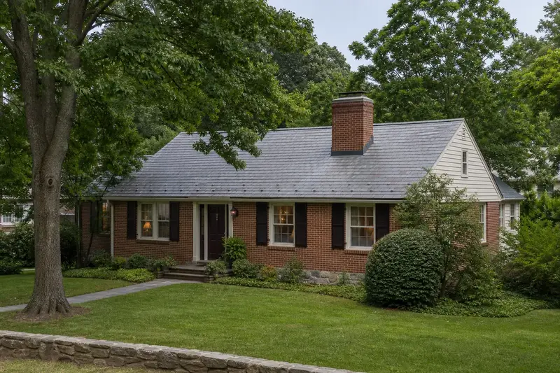 A 1990s brick rambler seen from the street with a red brick chimney with a concrete crown on a slate roof; illustrative image