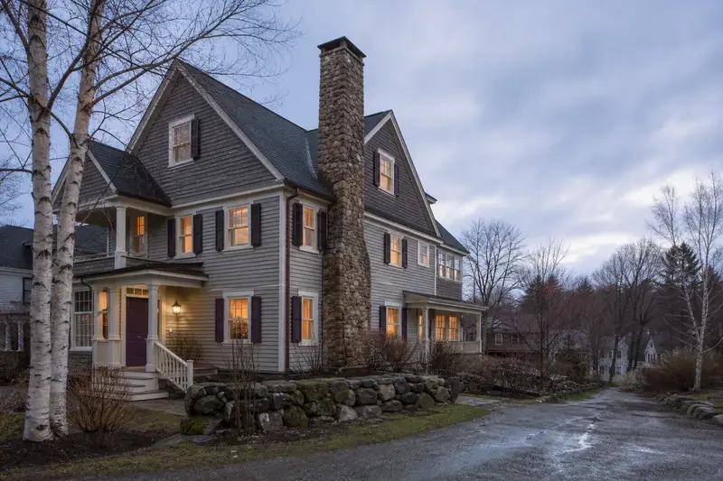 A 1940s triple-decker house in soft daylight with a stone masonry chimney standing clear above the roofline; illustrative image
