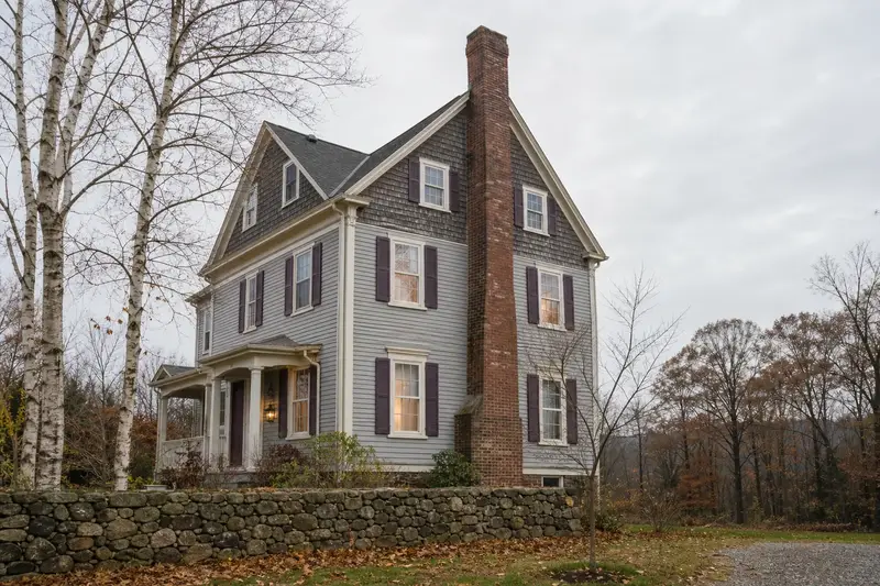 A 1920s triple-decker house with a tall brick chimney on a steep gable roof rising above a steep roof; illustrative image