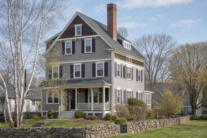 A 1950s triple-decker house in soft daylight with a tall brick chimney on a steep gable roof standing clear above the roofline; illustrative image