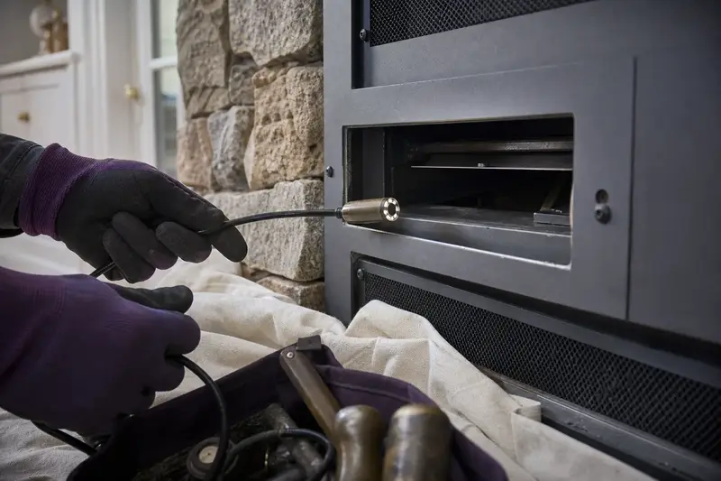 An inspection camera head on a flexible cable at the damper opening of a direct-vent gas fireplace; illustrative image