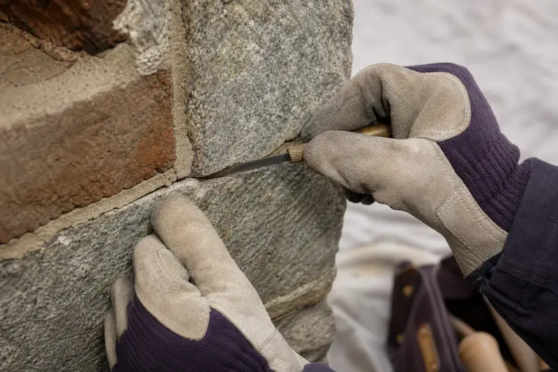 Gloved hands probing a cracked mortar joint with a thin feeler blade; illustrative image