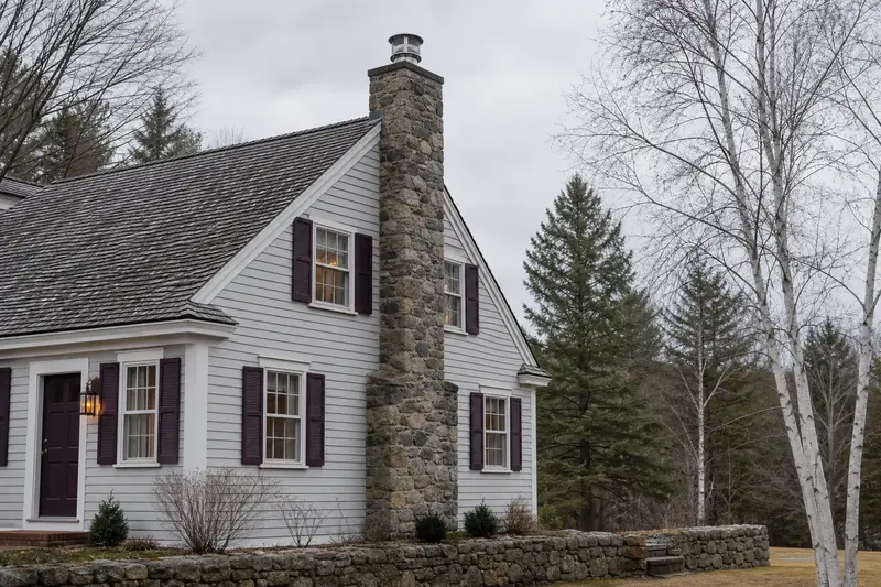 A 1940s clapboard colonial with a stone masonry chimney fitted with a stainless steel liner cap; illustrative image