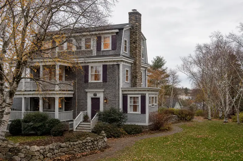 A 1950s triple-decker house in soft daylight with a stone masonry chimney standing clear above the roofline; illustrative image