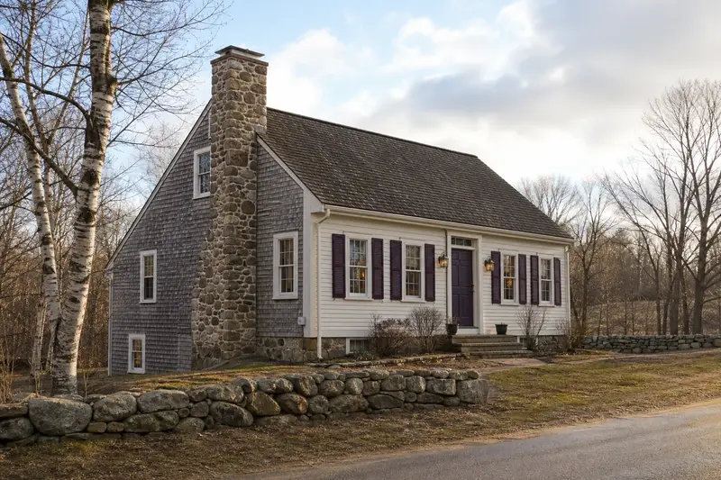 A 1950s saltbox house in soft daylight with a stone masonry chimney and even brickwork; illustrative image