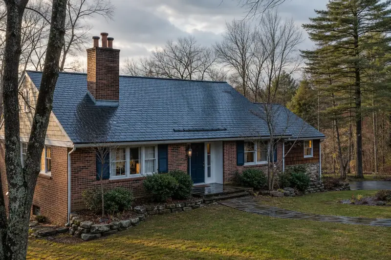 A 1970s brick-front ranch house after a cold rain with a two-flue brick chimney on a slate roof, wet roofs and clear gutters; illustrative image