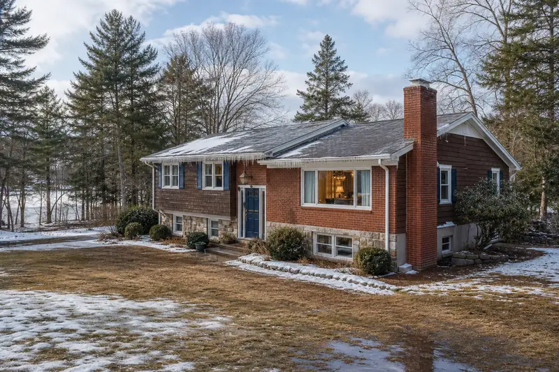 A 1990s split-level house on a thawing winter day with icicles at the eaves and a red brick chimney with a concrete crown; illustrative image