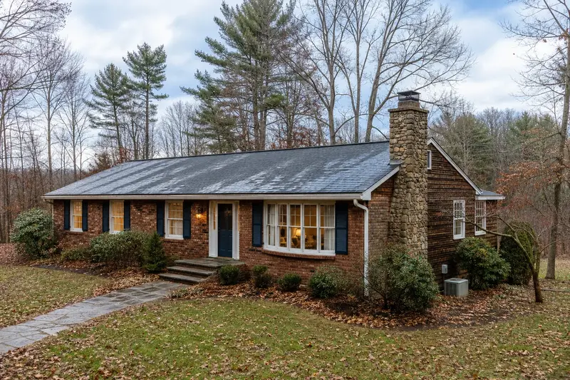 A 1960s brick-front ranch house after a cold rain with a stone masonry chimney, wet roofs and clear gutters; illustrative image