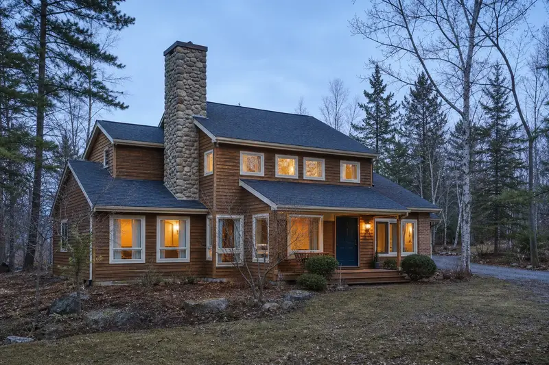 A 1980s cedar-sided contemporary house in soft daylight with a stone masonry chimney standing clear above the roofline; illustrative image