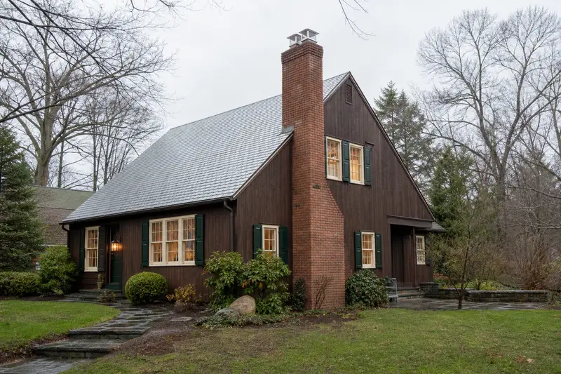 A 1970s cedar-sided contemporary house with a two-flue brick chimney on a slate roof topped by a new stainless steel cap; illustrative image