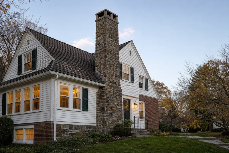 A 1950s Dutch colonial house in soft daylight with a stone masonry chimney standing clear above the roofline; illustrative image