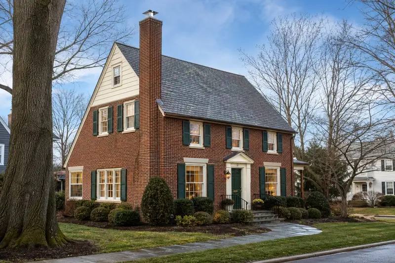 A 1950s brick colonial with a tall brick chimney on a steep gable roof topped by a new stainless steel cap; illustrative image