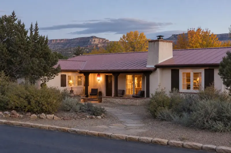 A 1970s stucco ranch house with a pitched metal roof with a stucco-finished chimney with a metal cap on a flat roof and a tidy front walk; illustrative image