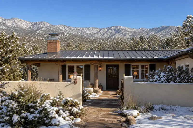 A 1980s single-story stucco house with a walled courtyard with a brick chimney with a spark arrestor cap on a metal roof topped by a stainless steel cap; illustrative image