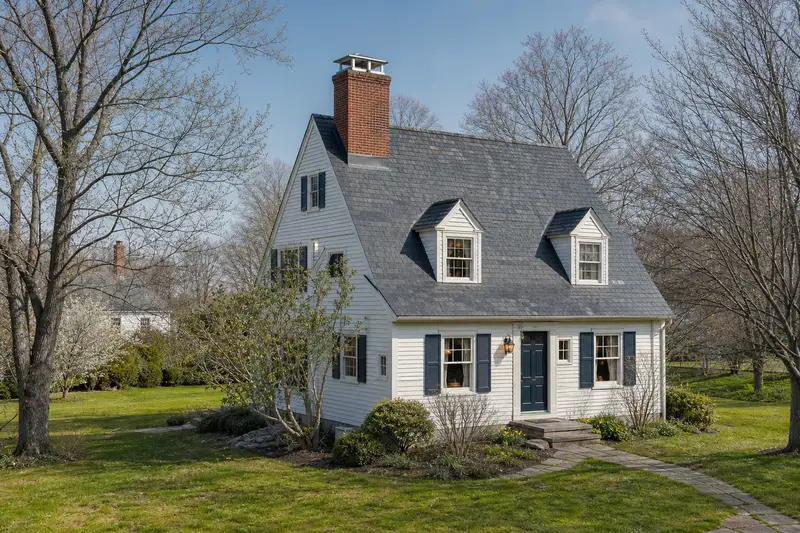 A 1940s steep-gabled frame house with a two-flue brick chimney on a slate roof topped by a new stainless steel cap; illustrative image