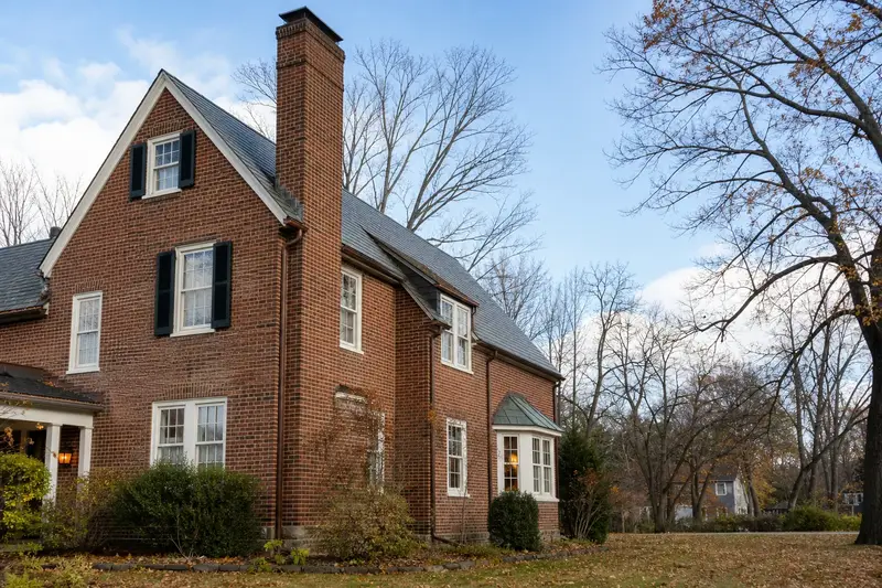 A 1930s brick two-story house with a tall brick chimney on a steep gable roof and neat mortar joints; illustrative image