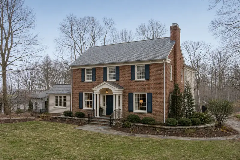 A 1930s brick two-story house in soft daylight with a red brick chimney with a concrete crown standing clear above the roofline; illustrative image