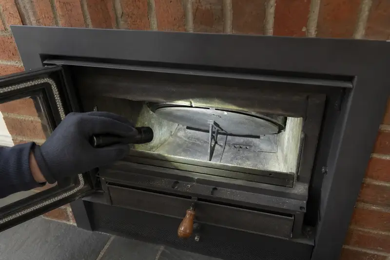 A flashlight beam across the smoke chamber and damper of a wood-burning insert in a brick opening, a gloved hand holding the light; illustrative image