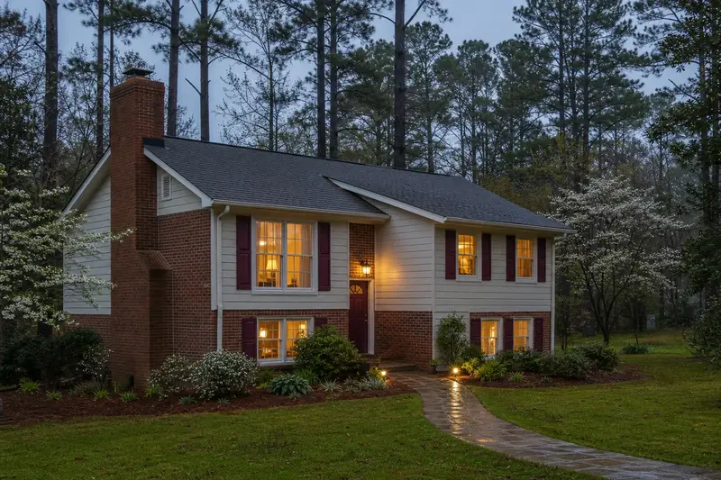 A 1990s brick-and-siding split-level house with an exterior end brick chimney on a gable roof, lit windows and a swept front walk; illustrative image