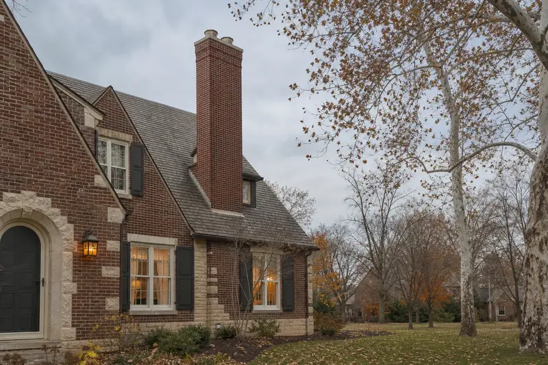 A 1940s Tudor revival house in soft daylight with a red brick chimney with a concrete crown standing clear above the roofline; illustrative image
