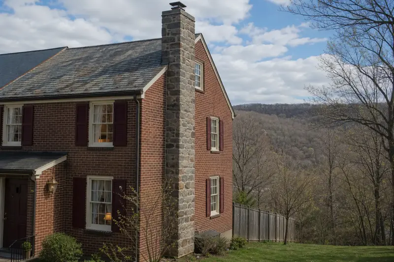 A 1950s brick rowhouse in soft daylight with a stone masonry chimney and even brickwork; illustrative image