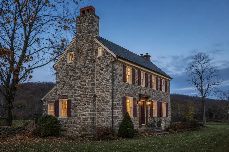 A 1940s stone farmhouse with a stone masonry chimney and neat mortar joints; illustrative image