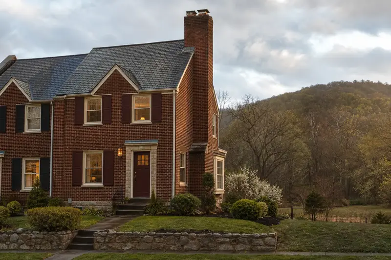 A 1940s brick rowhouse after a cold rain with a tall brick chimney on a steep gable roof, wet roofs and clear gutters; illustrative image