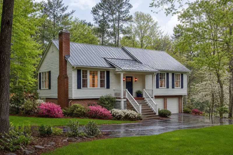 A 1980s raised coastal house with lap siding and a metal roof after a heavy rain with a red brick chimney with a concrete crown on a metal roof, wet roofs and clear gutters; illustrative image