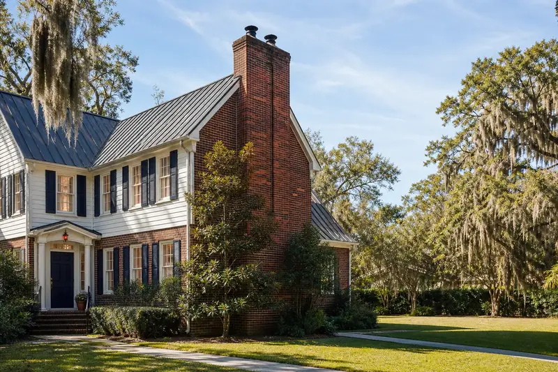 A 1970s two-story brick-and-siding suburban house with a two-flue brick chimney on a steep metal roof and a tidy front walk; illustrative image