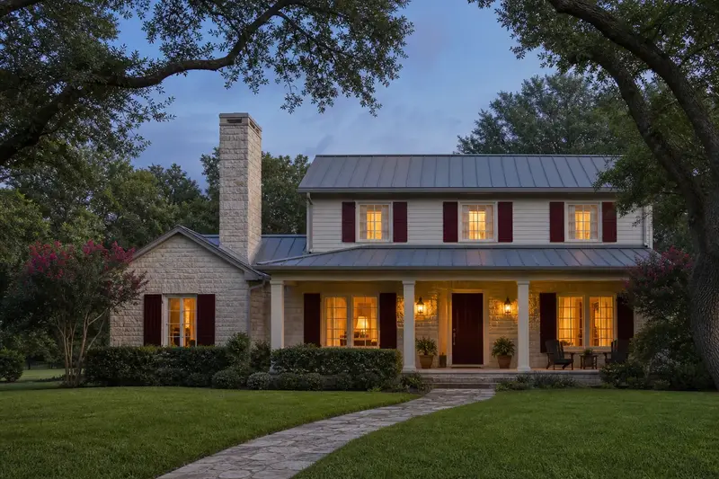 A 1990s limestone contemporary house with a metal roof with a limestone chimney with a concrete crown and warm lamp-lit windows; illustrative image