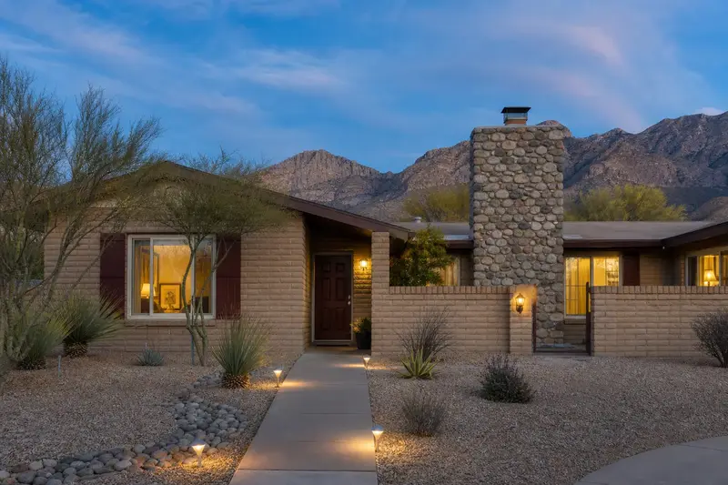 A 1980s single-story brick house with a courtyard wall with a river rock chimney with a spark arrestor cap and neat mortar joints; illustrative image