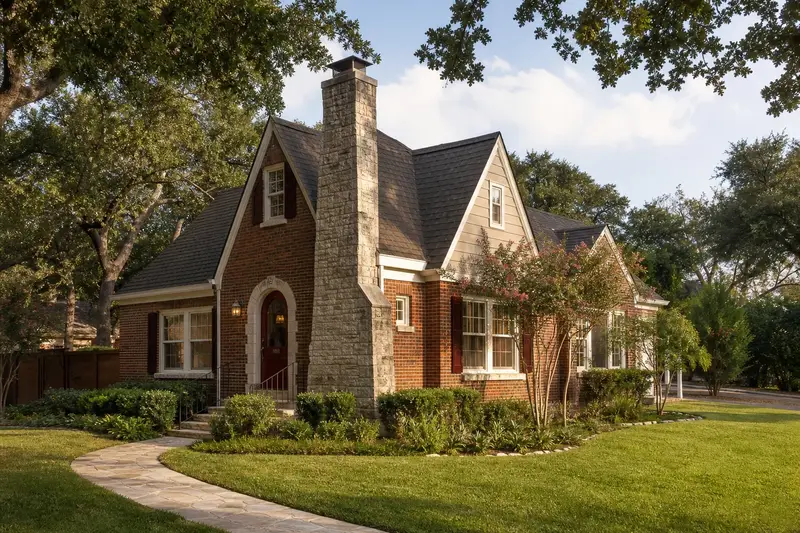 A 1920s brick Tudor revival cottage with a stone-veneer chimney with a steel cap and a tidy front walk; illustrative image