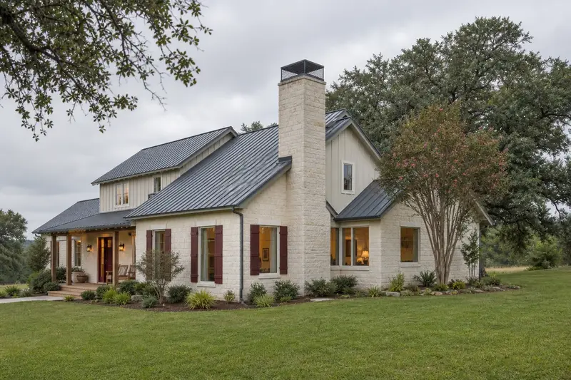 A 1980s limestone contemporary house with a metal roof with a limestone chimney with a concrete crown topped by a mesh chimney cap and mature trees nearby; illustrative image