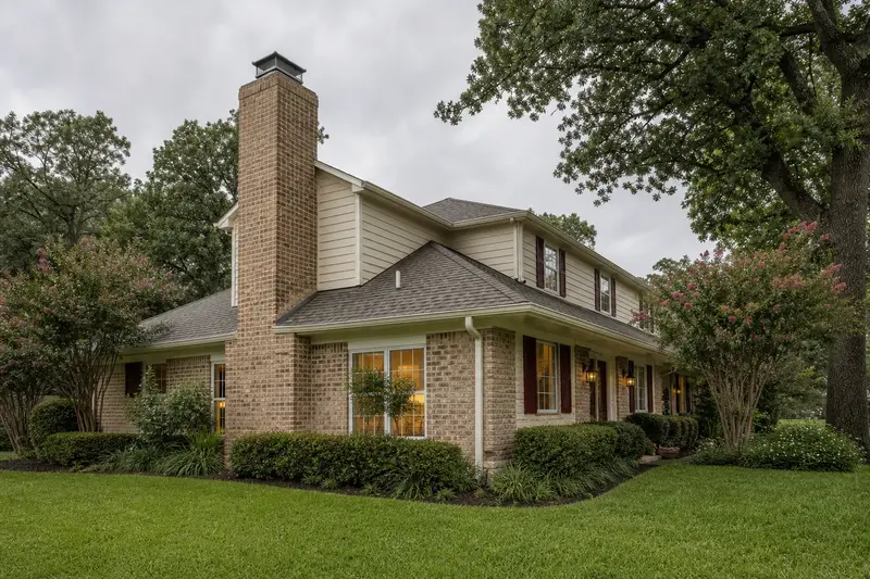 A 1980s brick-and-siding house with a hip roof with a tan brick chimney with a spark arrestor cap and neat mortar joints; illustrative image