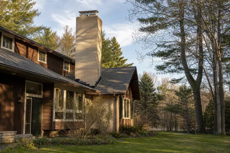 A 1970s cedar-sided contemporary house with a two-flue brick chimney on a slate roof topped by a new stainless steel cap; illustrative image