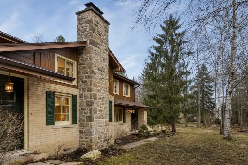 A 1970s two-story suburban house with a stone masonry chimney and neat mortar joints; illustrative image