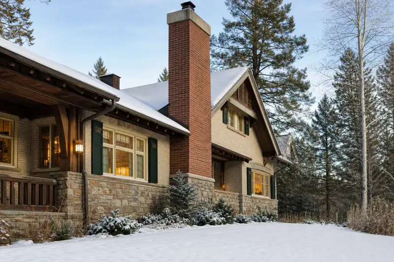 A 1950s Craftsman house with a red brick chimney with a concrete crown and warm windows as the heating season begins; illustrative image