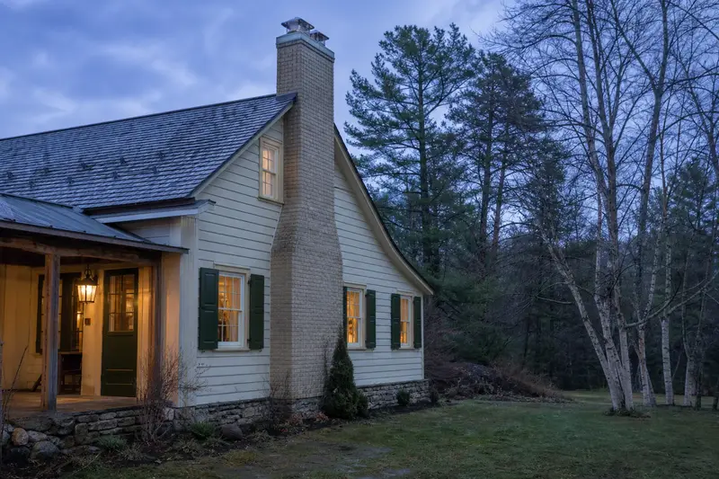A 1950s timber farmhouse with a two-flue brick chimney on a slate roof topped by a new stainless steel cap; illustrative image