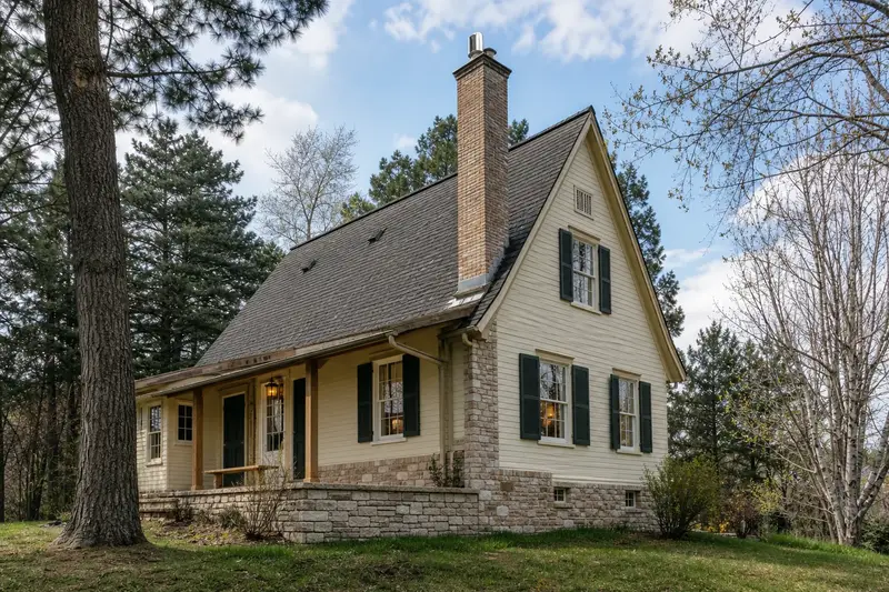 A 1950s timber farmhouse after steady rain with a tall brick chimney on a steep gable roof and a stainless steel cap; illustrative image